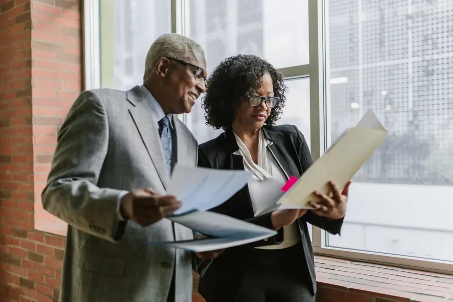 Two colleagues reviewing documents by an office window
